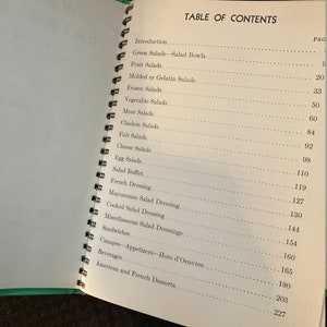 May include: A table of contents page from a vintage cookbook with a green cover. The page lists various salad recipes, including green salads, fruit salads, molded salads, frozen salads, vegetable salads, meat salads, chicken salads, fish salads, cheese salads, egg salads, salad buffet, French dressing, mayonnaise salad dressing, cooked salad dressing, miscellaneous salad dressings, sandwiches, canapes, appetizers, hors d'oeuvres, beverages, and American and French desserts.