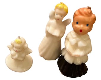 May include: Three vintage angel figurines. The angels have painted features, including blue eyes and red lips. One angel is wearing a black skirt. The figurines are made of a cream-colored material.