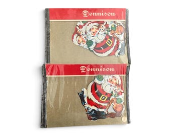 May include: Two vintage Dennison brand paper die-cut decorations in clear plastic packaging. Each features a colorful illustration of Santa Claus with a reindeer on a tan background, topped with a red header strip displaying the Dennison logo.