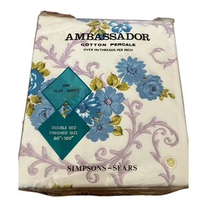 May include: A packaged Ambassador cotton percale flat sheet for a double bed. The sheet is white with a floral pattern in blue, yellow, and purple. The package reads "Double Bed Finished Size 203cm x 254cm" and "Simpsons-Sears."