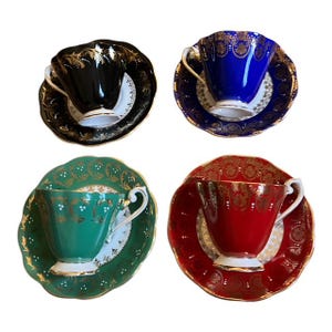 May include: Four vintage teacups and saucers in black, blue, green, and red. Each cup and saucer has gold detailing. The teacups have white interiors and delicate handles. A classic set for afternoon tea or display, with a touch of elegance.