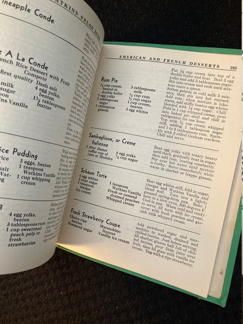 May include: A vintage cookbook open to a page with recipes for American and French desserts. The page features recipes for Rum Pie, Sambaglione, or Creme Italienne, Schaum Torte, Fresh Strawberry Coupe, and more.