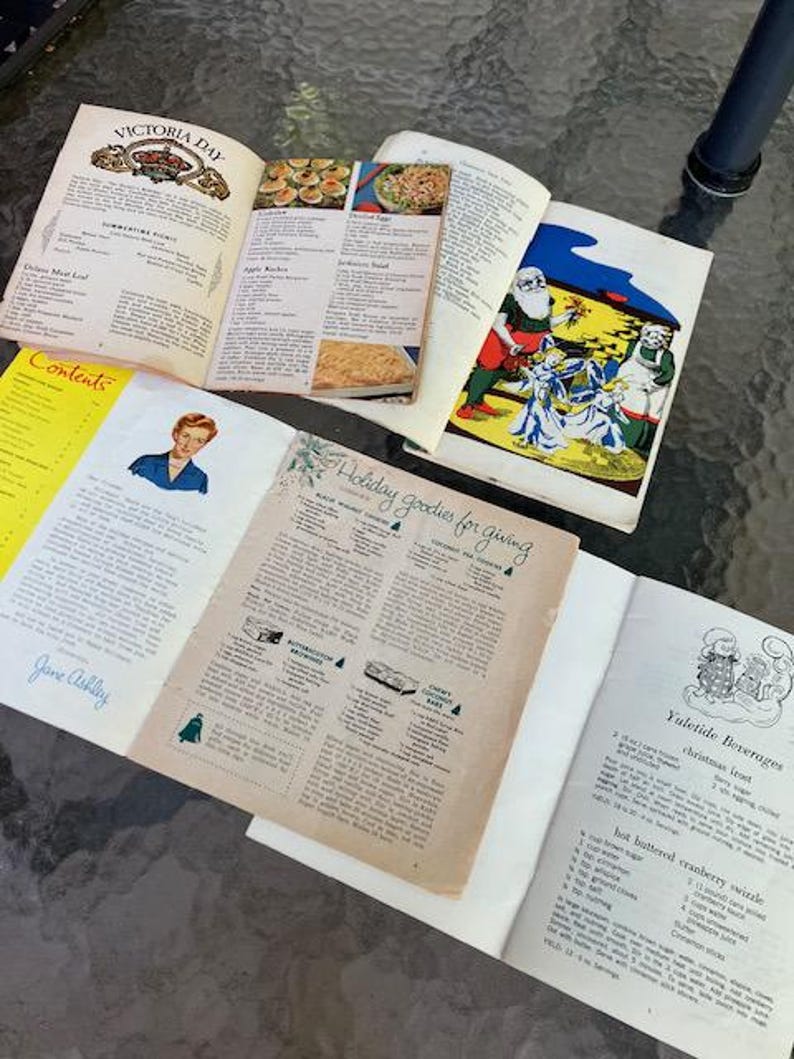 May include: Open vintage cookbooks with recipes for Victoria Day and holiday treats. One page features a Santa Claus illustration. The text includes "Holiday goodies for giving" and "Yuletide Beverages".