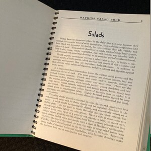 May include: A vintage Watkins Salad Book with a green cover and a spiral binding. The book features a title page with the words "Watkins Salad Book" and the number "5" in the top right corner. The page also includes a section titled "Salads" with text about the importance of salads in a healthy diet.
