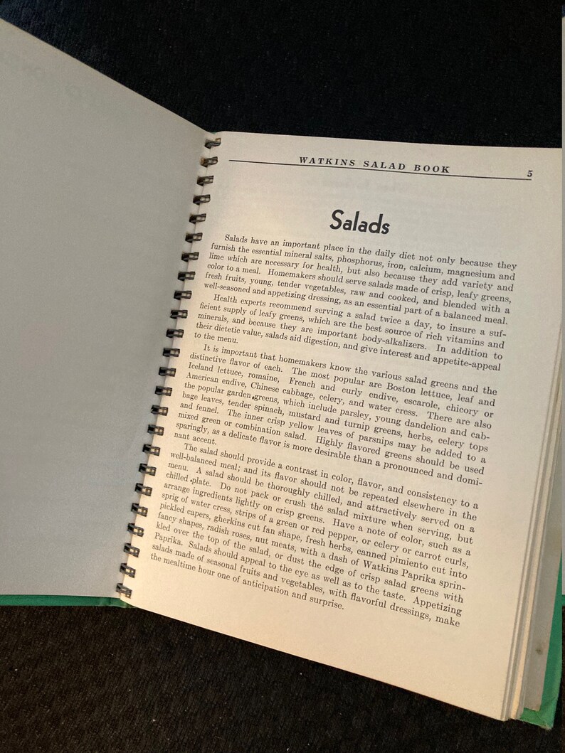 May include: A vintage Watkins Salad Book with a green cover and a spiral binding. The book features a title page with the words "Watkins Salad Book" and the number "5" in the top right corner. The page also includes a section titled "Salads" with text about the importance of salads in a healthy diet.