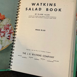 May include: A vintage Watkins Salad Book with a green cover and a spiral binding. The book is open to the title page, which features the title "Watkins Salad Book" in large, bold letters. The author, Elaine Allen, is listed below the title, along with the price, $1.50. The copyright information is at the bottom of the page, indicating the book was published in 1946 by The J. R. Watkins Company.