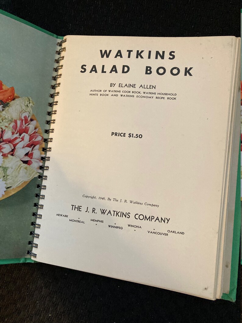 May include: A vintage Watkins Salad Book with a green cover and a spiral binding. The book is open to the title page, which features the title "Watkins Salad Book" in large, bold letters. The author, Elaine Allen, is listed below the title, along with the price, $1.50. The copyright information is at the bottom of the page, indicating the book was published in 1946 by The J. R. Watkins Company.