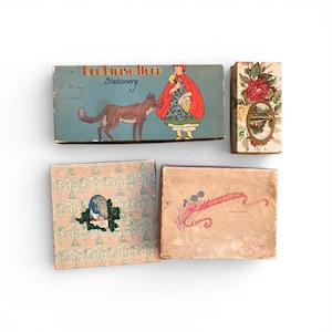 May include: A selection of vintage stationery boxes. One box features a Red Riding Hood illustration with a wolf. Other boxes display floral and decorative designs, with text on some. The boxes are in various sizes and shapes.