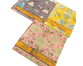 May include: Three sheets of gift wrap with different patterns. One has a gray background with illustrations of women in dresses, another has a yellow background with a floral design, and the third has a light green background with pink roses.