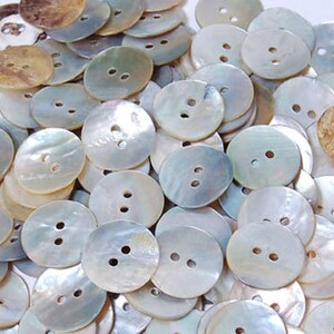 May include: A collection of white and brown oval-shaped buttons made from mother of pearl. The buttons have two holes each.