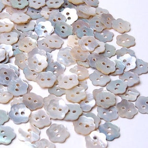 Può includere: Un grande mucchio di bottoni bianchi, iridescenti, a forma di fiore con due fori ciascuno.