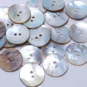 Może przedstawiać: Zbiór białych i brązowych guzików z perłowej masy perłowej z dwoma lub trzema otworami. Guziki są okrągłe i mają gładkie, błyszczące wykończenie.