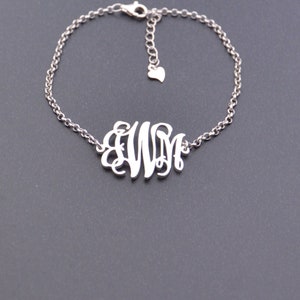 Puede incluir: Un brazalete de cadena de plata con un dije de monograma con las letras "WM".
