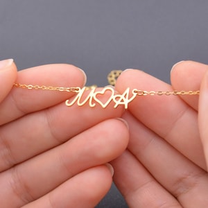 May include: Gold necklace featuring a heart and two initials, "M" and "A", linked together.