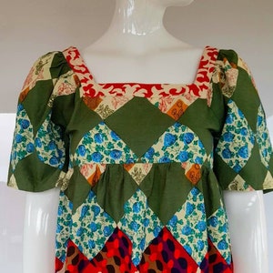 Puede incluir: Una blusa de patchwork verde, rojo, azul y blanco con escote cuadrado y mangas abullonadas cortas. La blusa tiene un patrón geométrico y está hecha de algodón.