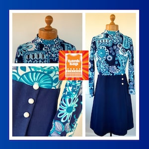 Puede incluir: Un vestido estampado en azul y blanco con cuello alto y mangas largas. El vestido tiene una falda azul marino y botones blancos en la parte delantera. El vestido está en un maniquí y el fondo es una pared blanca.