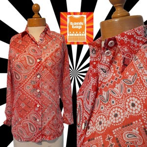 May include: A red and white paisley print long-sleeved button-up shirt. The shirt has a classic collar and a relaxed fit. The print is reminiscent of a bandana.