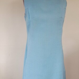 May include: A sleeveless light blue dress with a round collar. The dress is on a mannequin.