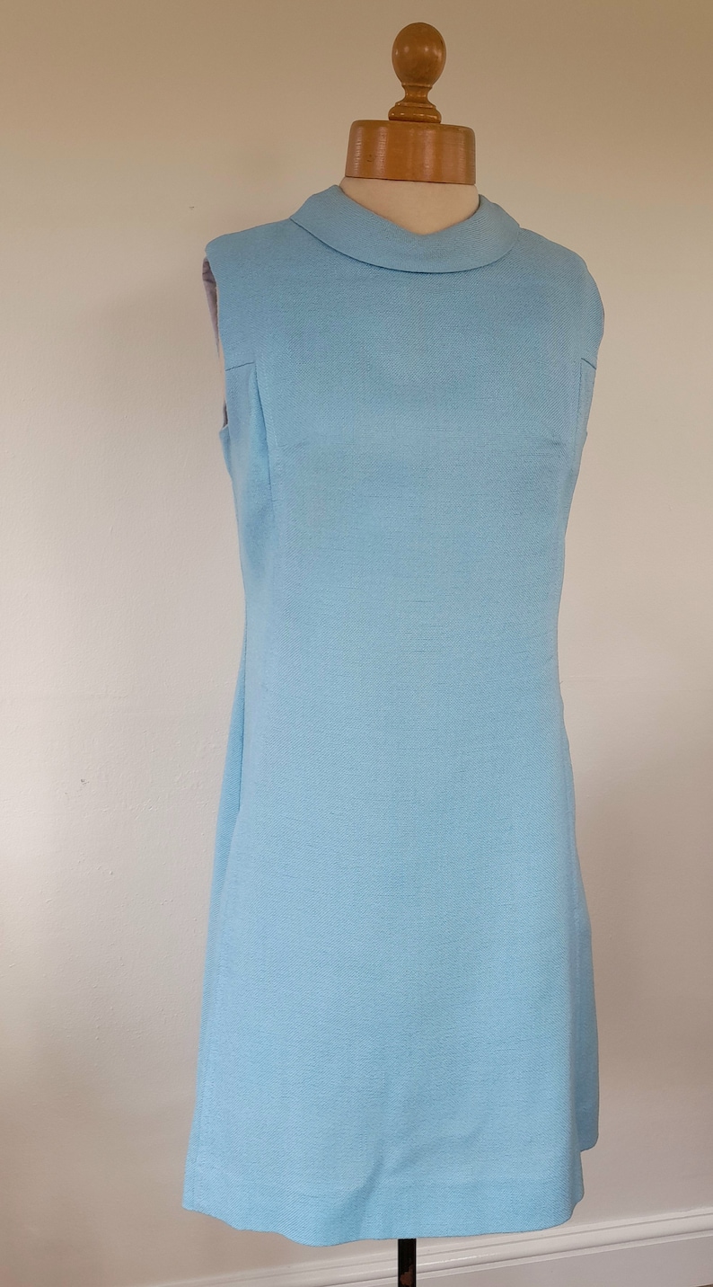 May include: A sleeveless light blue dress with a round collar. The dress is on a mannequin.