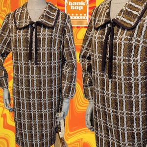 May include: A vintage brown, white, and tan plaid dress with a rounded collar and a dark brown tie. The dress is displayed on a mannequin. A straw handbag with a wooden handle is visible. The image includes a logo that says "Tank Top Vintage".