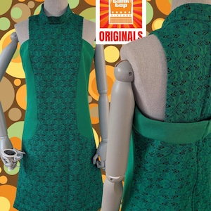 May include: A sleeveless green dress featuring a high mock neck and a central panel with a black intricate pattern. The sides are solid green, and the garment is displayed on a mannequin. A logo with the text Tank Top Vintage Originals is visible.