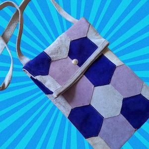 May include: A patchwork crossbody bag with a geometric design. The bag features a combination of purple, blue, and off-white suede pieces. It has a long strap and a silver button closure. The bag's dimensions are not visible.