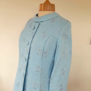 May include: A light blue dress with a circular pattern. The dress has a collar and long sleeves.