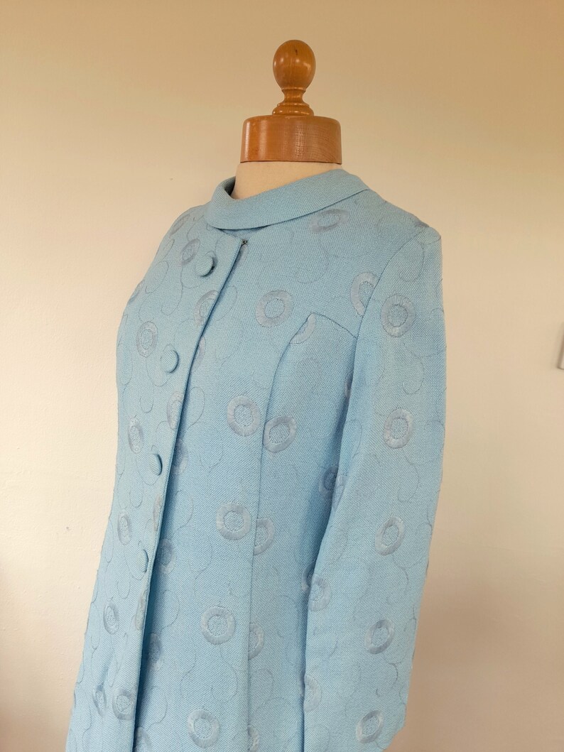 May include: A light blue dress with a circular pattern. The dress has a collar and long sleeves.