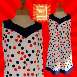 May include: A vintage sleeveless dress featuring a white base with red and navy blue polka dots. The dress has a navy blue V-neck and trim. The Tank Top Vintage logo is in the upper right corner.
