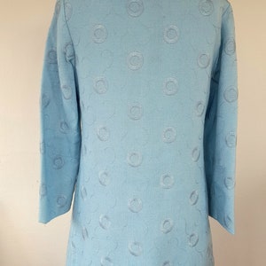 May include: A light blue dress with a white collar and a pattern of embroidered circles. The dress has three-quarter sleeves and a slightly flared skirt.