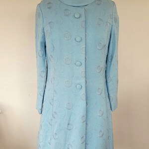 May include: A light blue dress with a round, embroidered pattern and button fastening. The dress has long sleeves and a fitted silhouette.