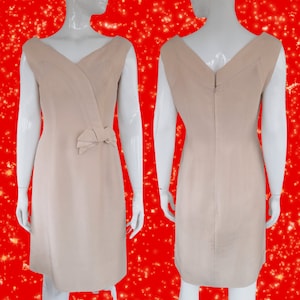 May include: A sleeveless, light beige dress with a V-neckline and a bow detail at the waist.