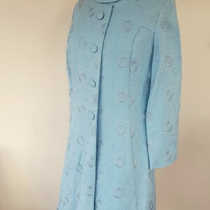May include: A light blue dress with a round, embroidered pattern. The dress has a collar and a button-up front.