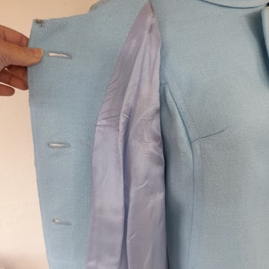May include: A light blue dress with a collared neckline and a button-up front. The dress has a light blue lining that is visible through the open front.