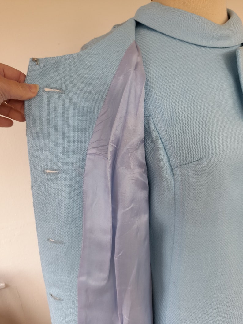 May include: A light blue dress with a collared neckline and a button-up front. The dress has a light blue lining that is visible through the open front.