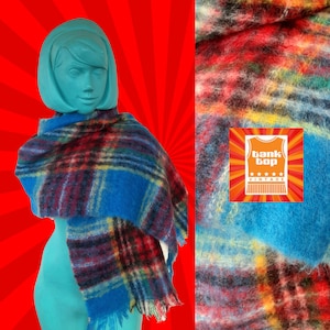May include: A blue and red plaid scarf with fringed edges. The scarf is made of a soft, fuzzy material. The scarf is draped over a mannequin's shoulders.
