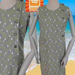 May include: A sleeveless grey dress with a green and white pattern. The dress features a button closure and a small pocket. The dress is displayed on a mannequin with a beach backdrop. The logo "Bank Top Vintage" is in the top corner.