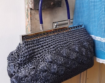 May include: A black woven handbag with a blue handle and a floral design. The bag is closed and has a metal clasp.