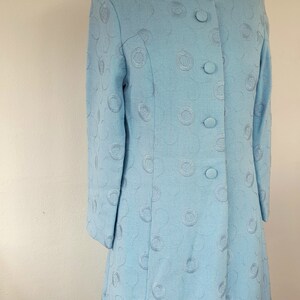 May include: A light blue dress with a round, embossed pattern. The dress has a collared neckline and a button-up front.