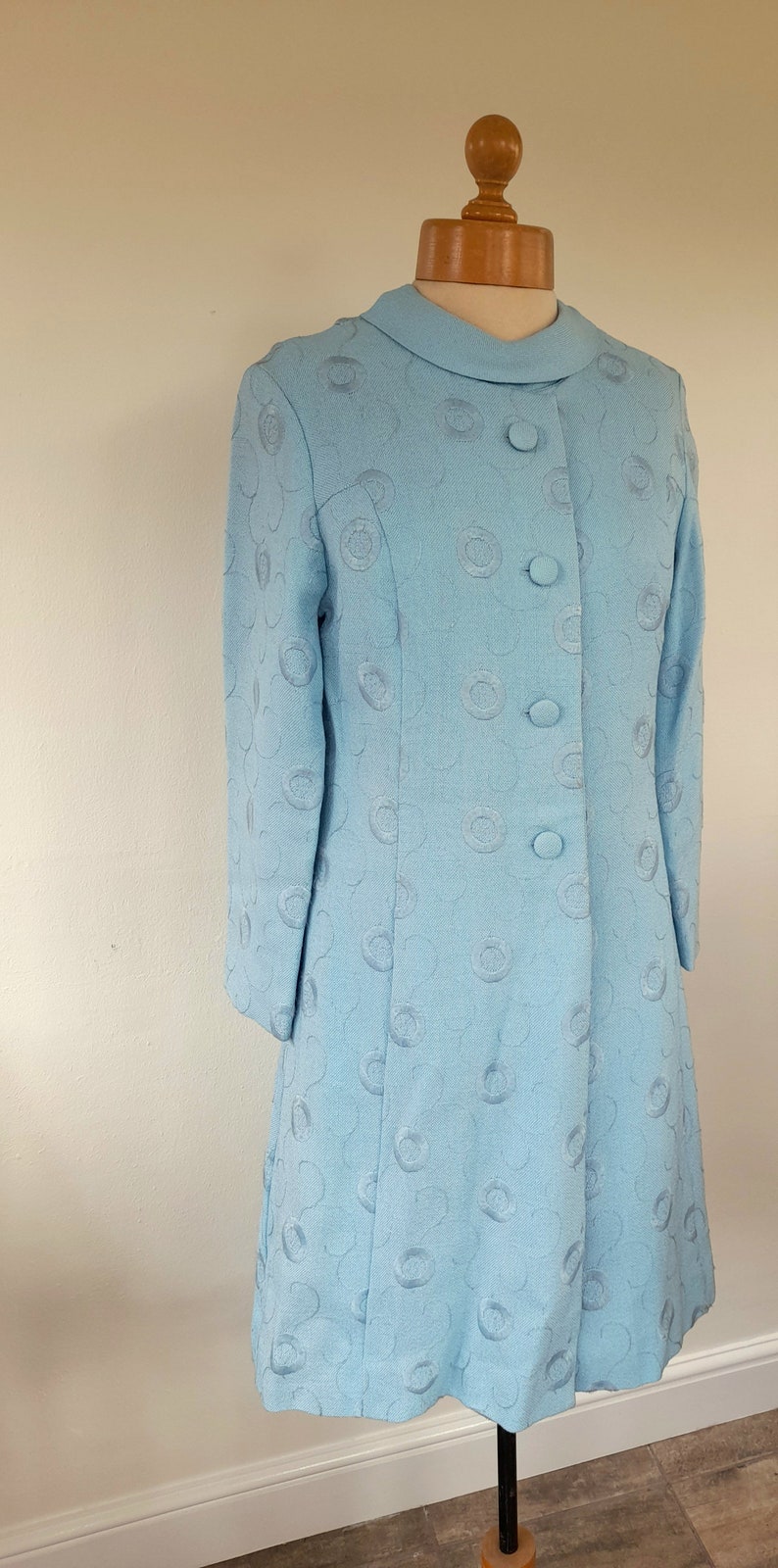 May include: A light blue dress with a round, embossed pattern. The dress has a collared neckline and a button-up front.