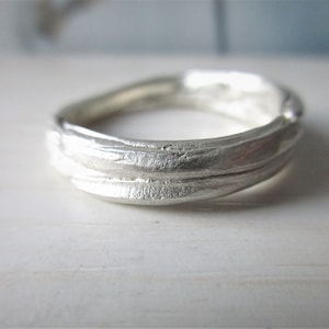 Könnte beinhalten: Ein silberner Ring mit einem strukturierten, organischen Design. Der Ring besteht aus zwei Bändern, die miteinander verdreht sind.