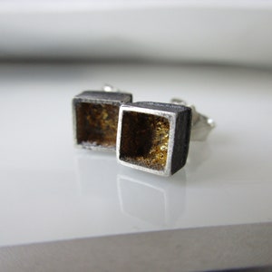 May include: A pair of silver square earrings with a gold interior. The earrings have a textured surface.