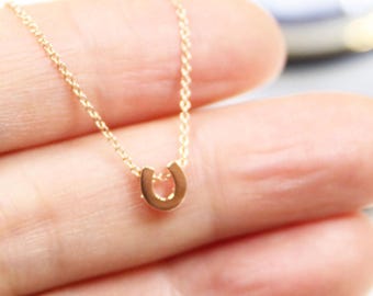 Puede incluir: Un collar de cadena de oro con un pequeño colgante de herradura. El collar está en la mano de una persona.