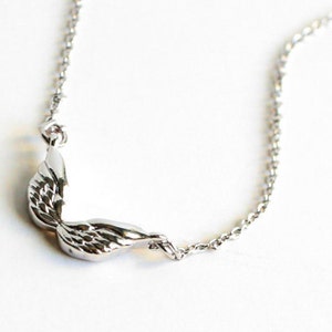 May include: A silver necklace featuring a delicate wing pendant. The wings are detailed and have a slightly curved shape.