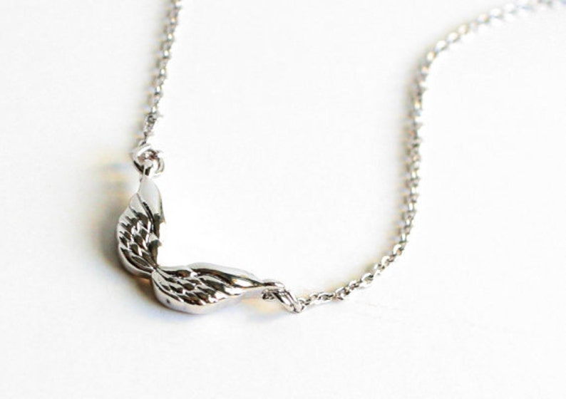May include: A silver necklace featuring a delicate wing pendant. The wings are detailed and have a slightly curved shape.