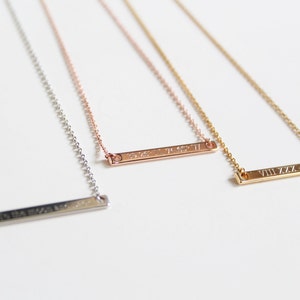 May include: Three silver bar necklaces with different Roman numeral engravings. The necklaces are on a white background.