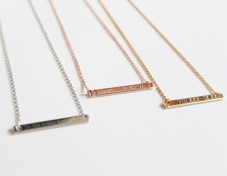 May include: Three silver bar necklaces with different Roman numeral engravings. The necklaces are on a white background.