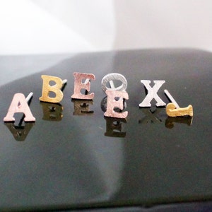 May include: A set of six gold, silver and rose gold letter earrings. The letters are A, B, E, E, X and J.