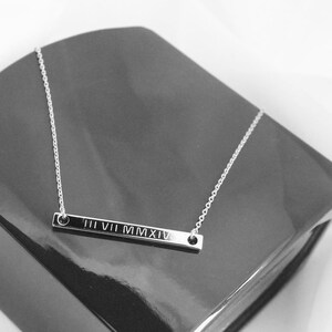 May include: A silver necklace with a bar pendant engraved with the Roman numerals III VII MMXIV.
