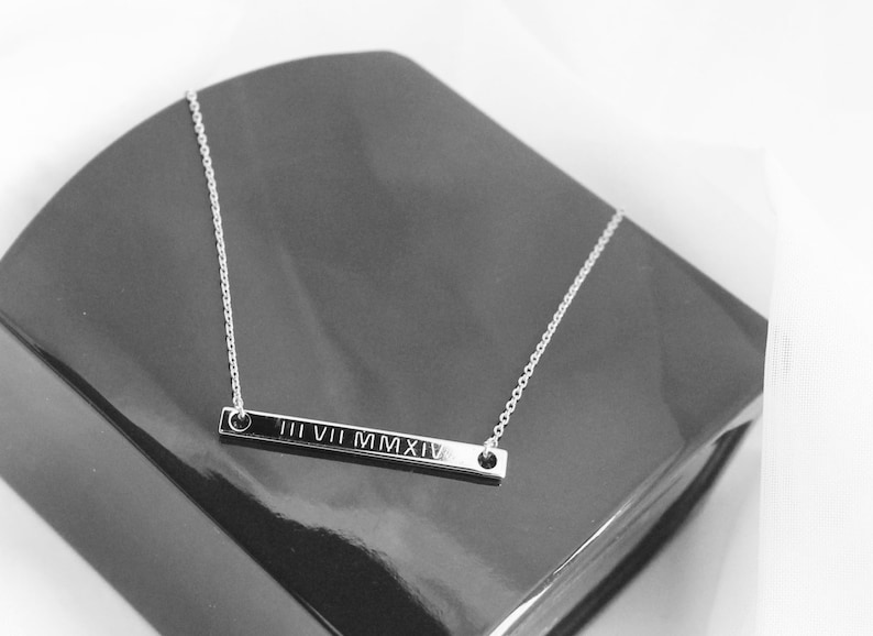 May include: A silver necklace with a bar pendant engraved with the Roman numerals III VII MMXIV.